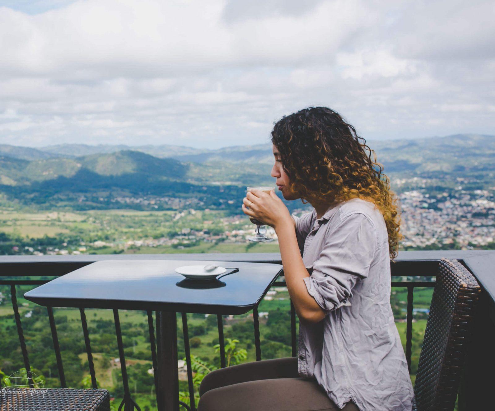 A woman sitting and drinking coffee at a restaurant on Jamaca de Dios with the view of the mountains in the background.