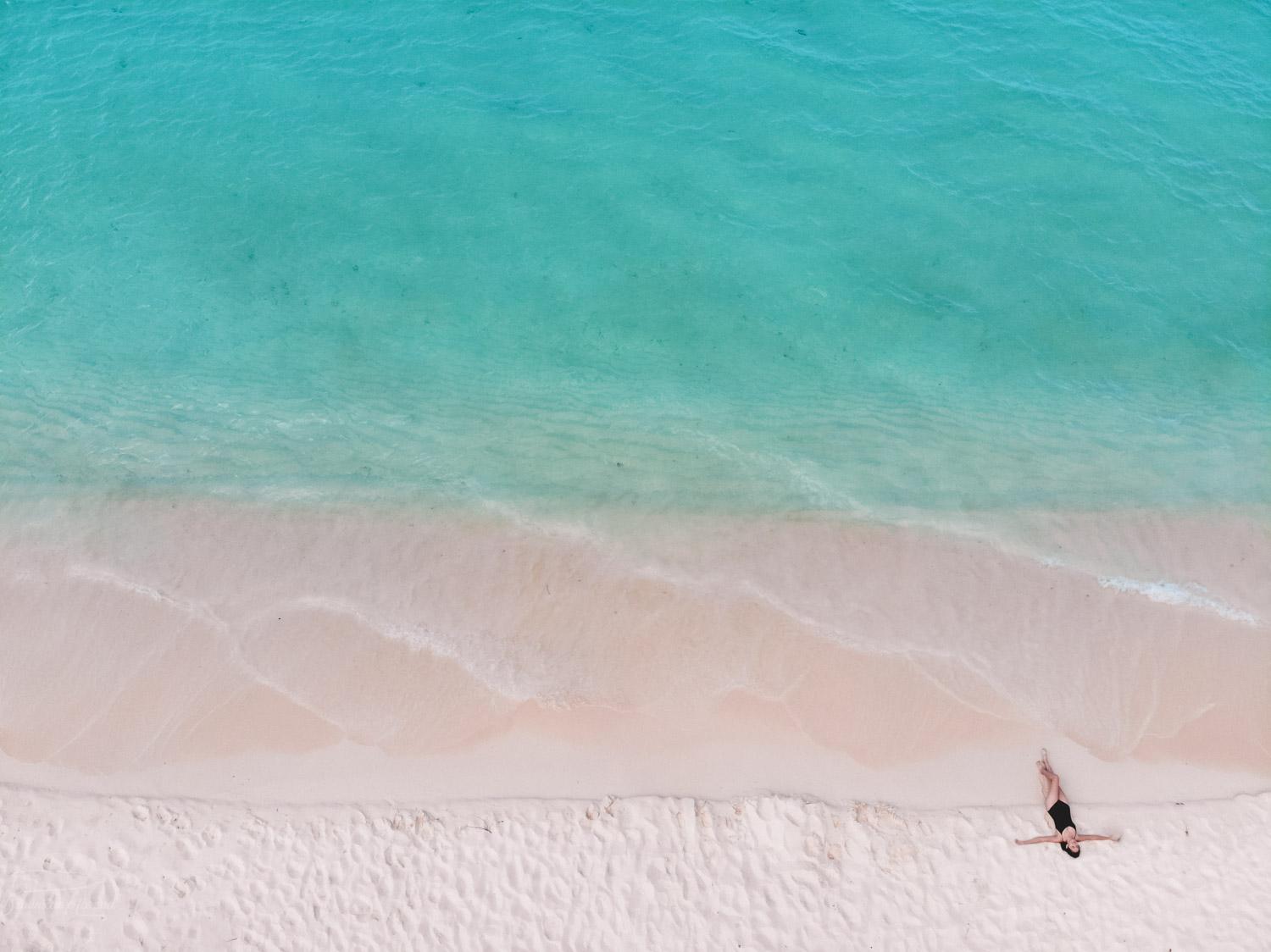 A woman lying down on the beautiful white sand near the turquoise water of Bahia de las Aguilas beach.