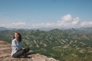 A woman sitting on a rock ground overlooking mountains of haiti