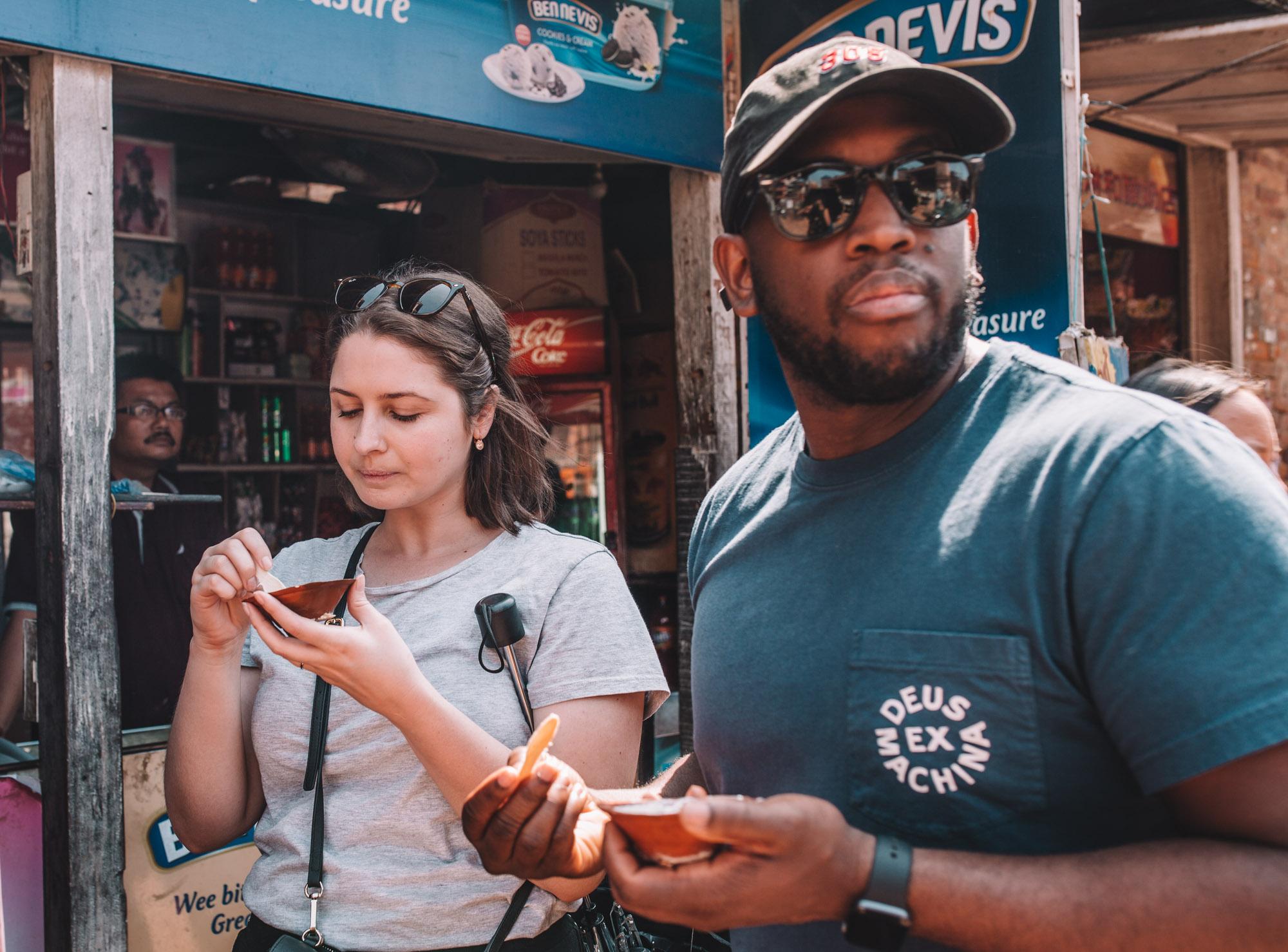 A man and a woman walking on a street having Bhaktapur yogurt curd.