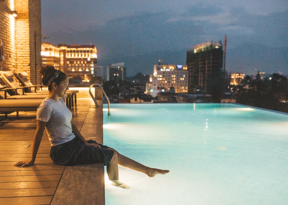 A woman sitting at the edge of an outdoor rooftop swimming pool at Hotel Mulberry in Kathmandu.