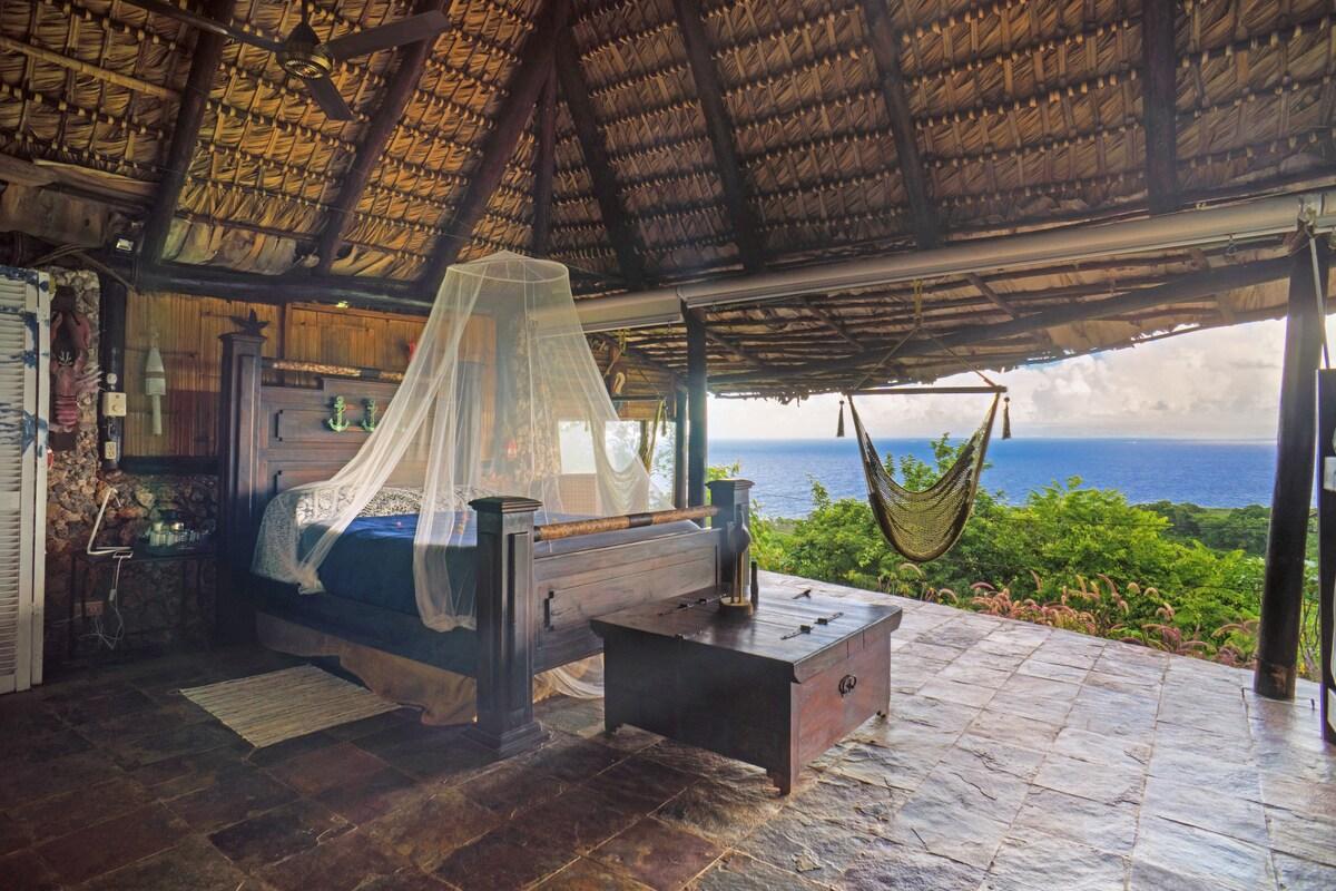 A bed in an big open hut overlooking trees and the sea in the Dominican Republic.