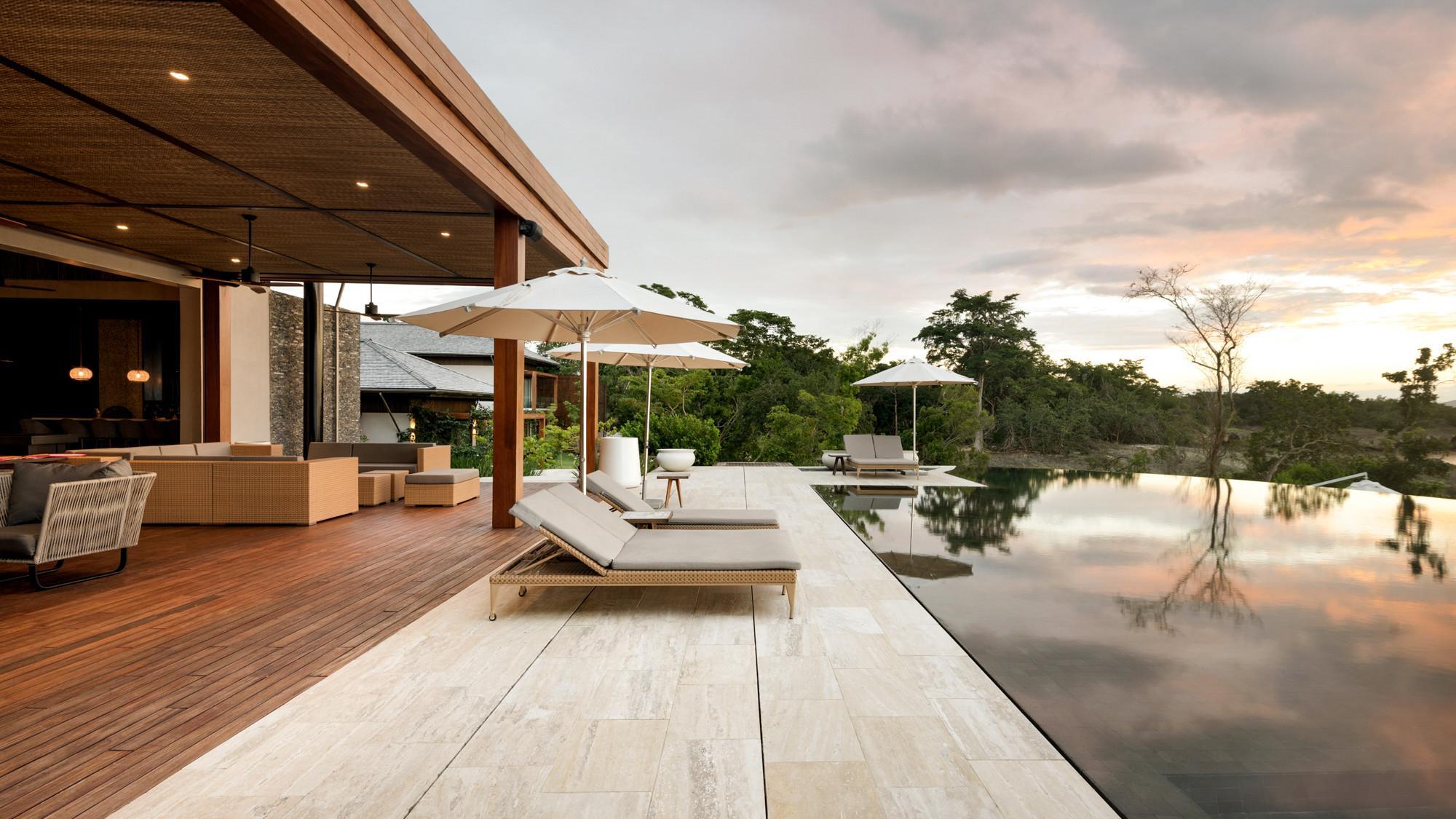 A luxurious swimming pool area with chairs at a villa surrounded by trees in the Dominican Republic.