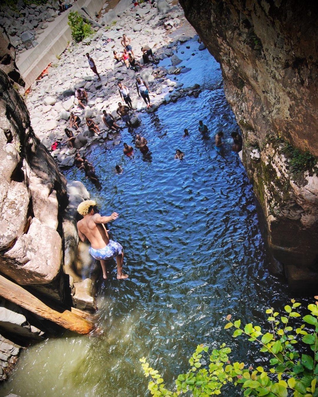 A man jumping into a waterfall's natural pool.