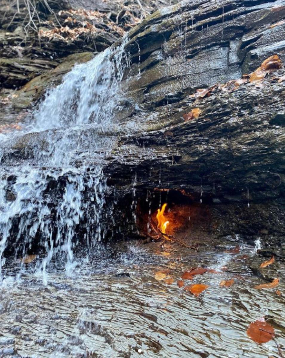 A waterfall near a small grotto with a flame.