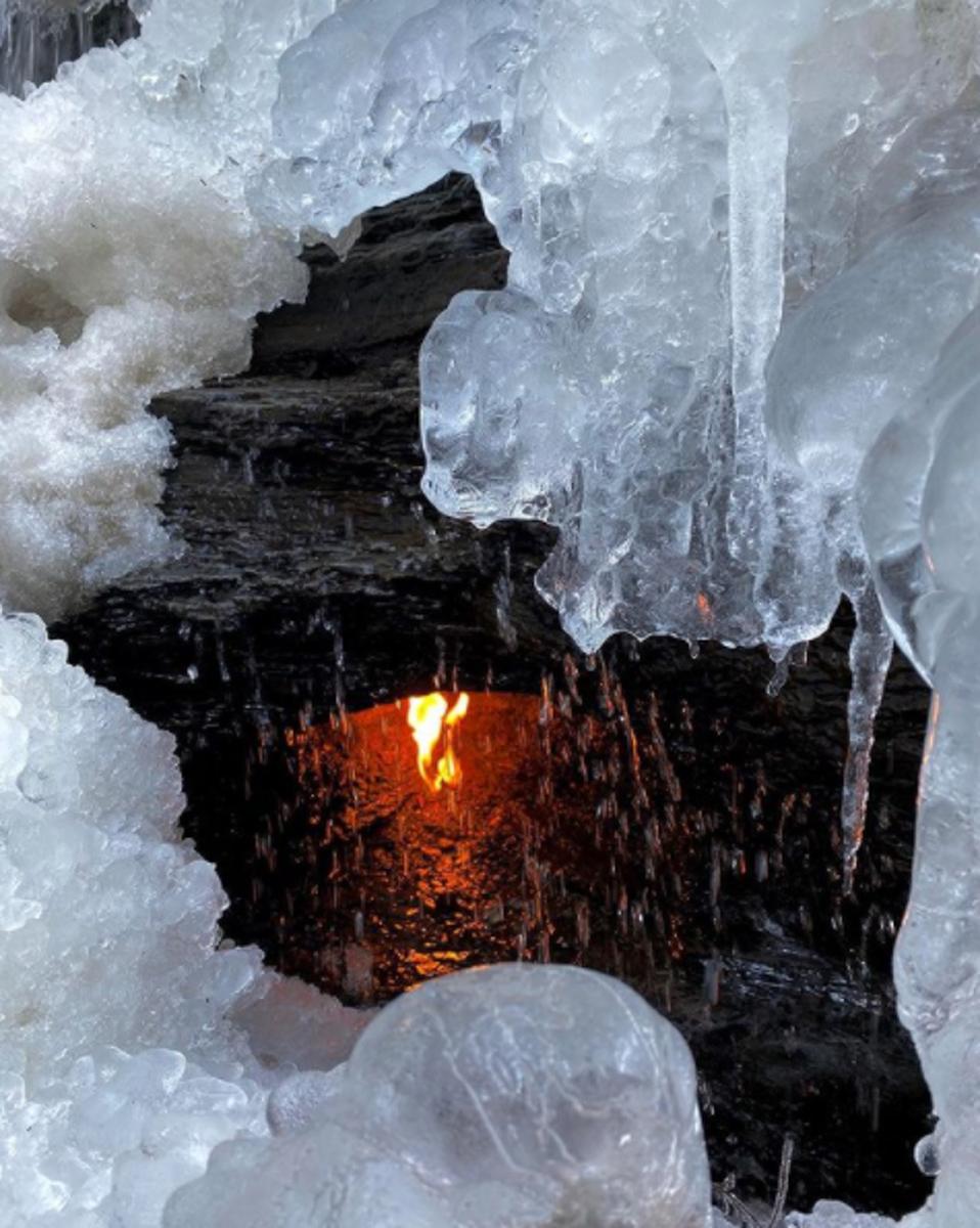 A small grotto with a flame partially surrounded by frozen waterfalls.
