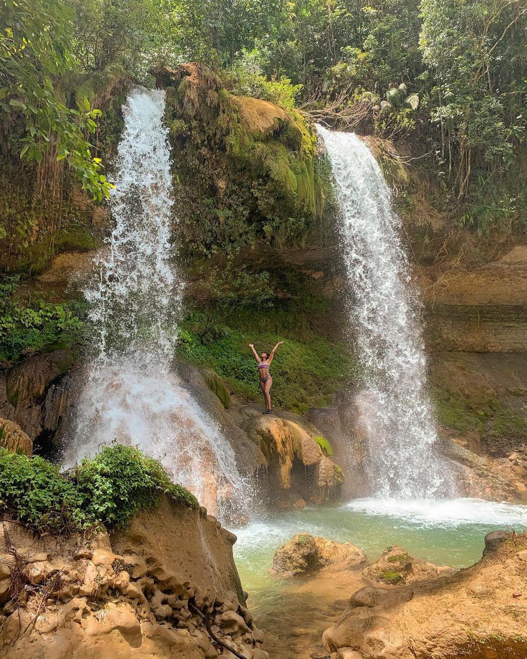 A woman standing between two waterfalls in the Dominican Republic.