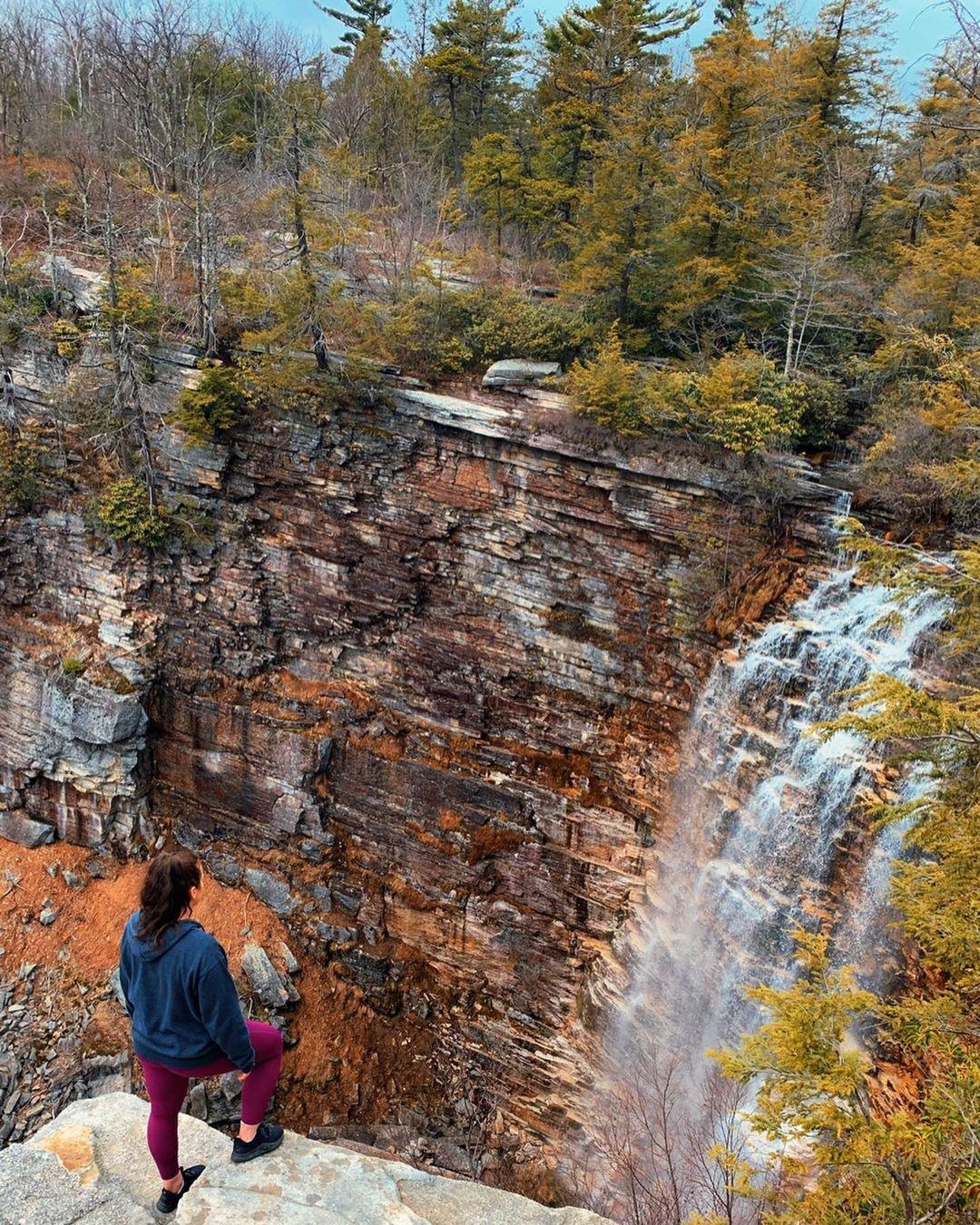A woman standing on a high ground and looking at the waterfall in front of her.
