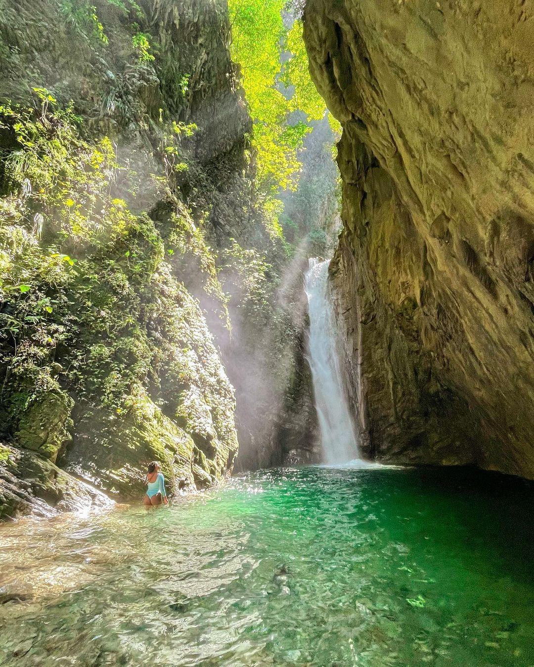 A woman admiring the La Taína Waterfall as the sunlight shines through it.