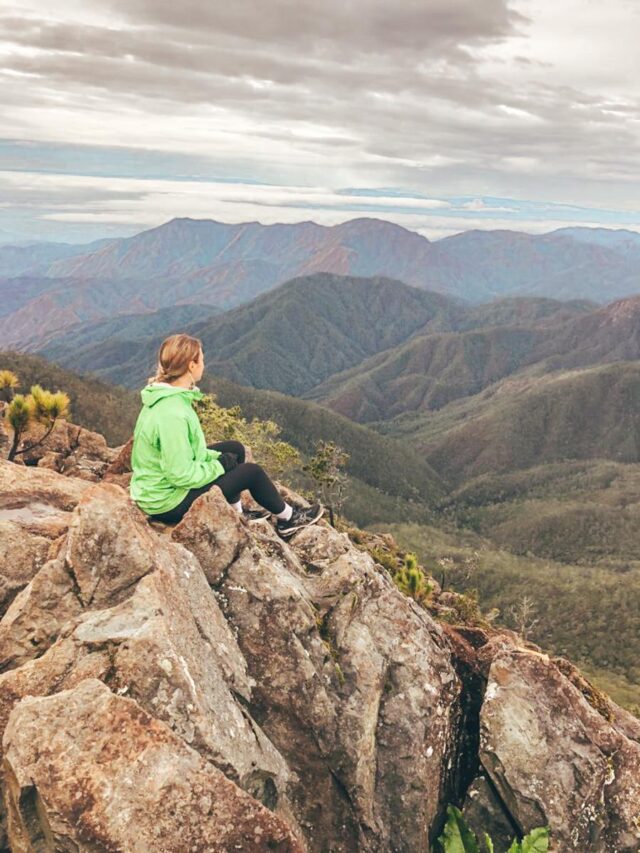 A woman in green jacket sitting on giant rocks while looking at the Dominican Alps.