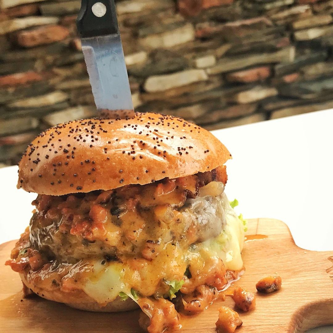 Burger with knife in the middle on a chopping board.