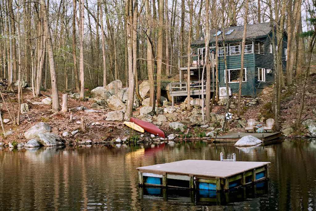 A lakefront green log cabin in the woods.