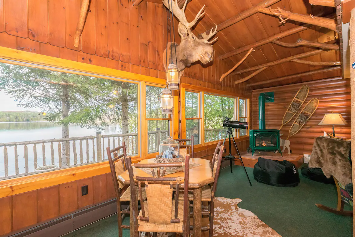 A waterfront cabin with fireplace, tables, chairs, and decorations.