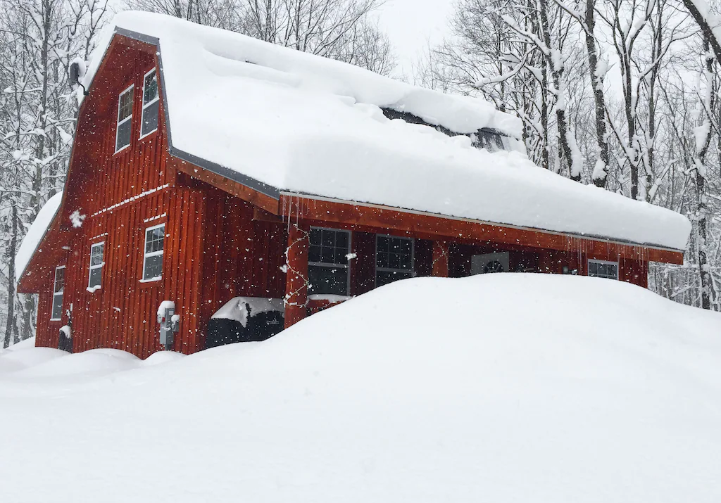 A red cabin partly covered by snow in winter.