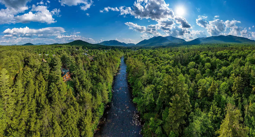 A view of a river between trees and mountains from afar.