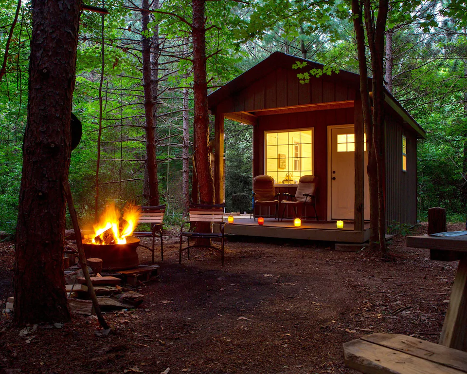 A tiny cabin in the woods with a bonfire area.