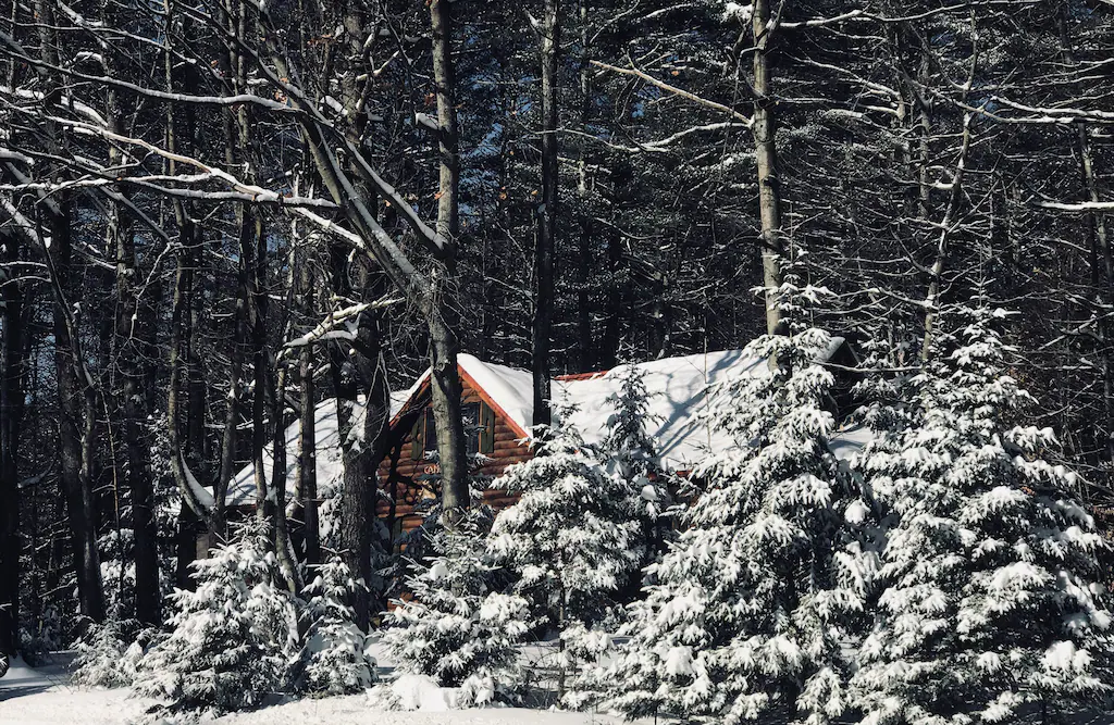 A log cabin in the woods partly covered by snow in winter.