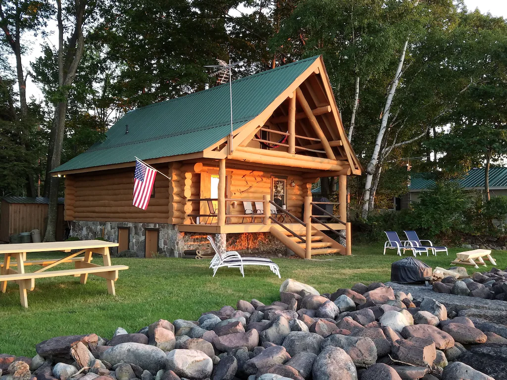 A log cabin surrounded by trees and big rocks.