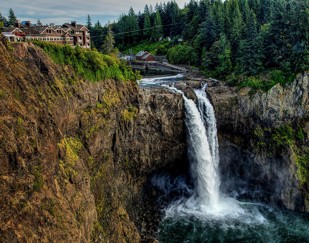 Twin waterfalls cascade with houses in the background.