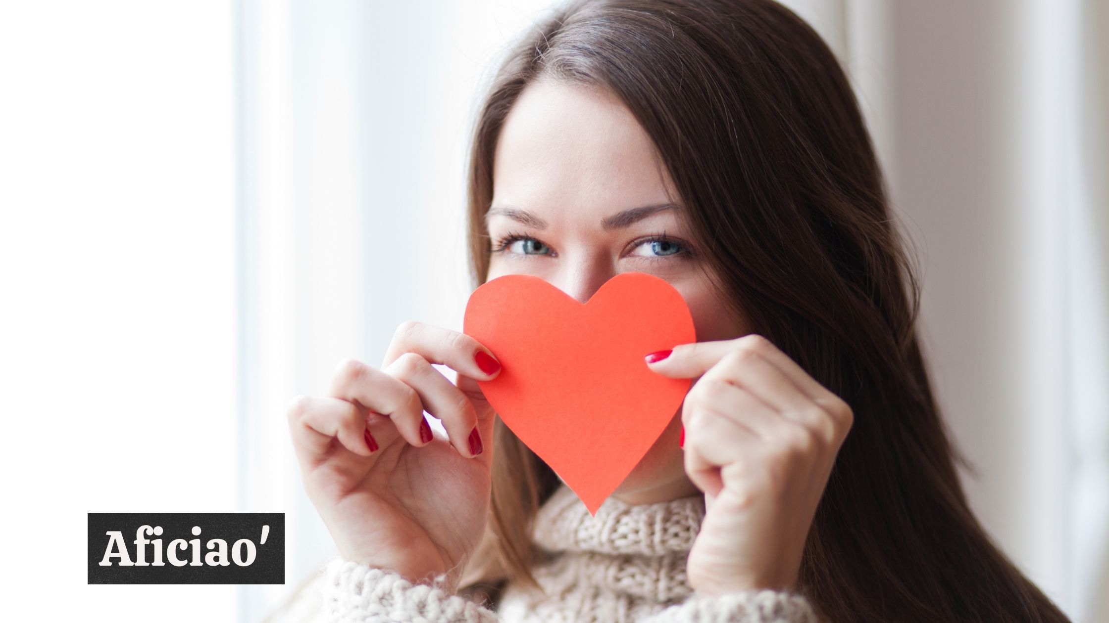 A woman covering her face with a red paper heart; "Aficiao'" text in image.