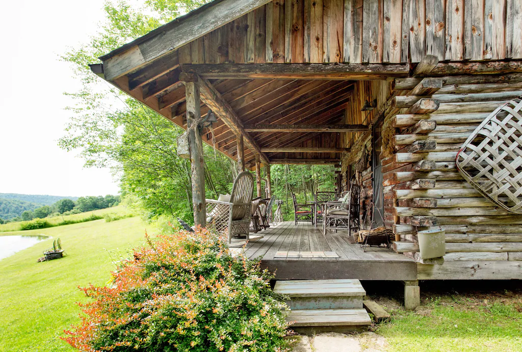 A log cabin with wooden furniture near a pond.