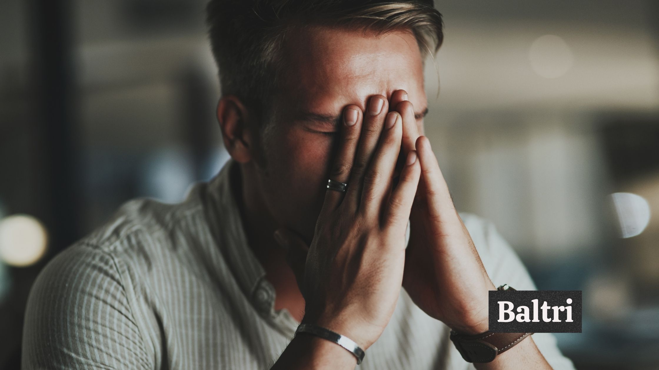 A man learning his face on his hands positioned on a prayer-like position; "Baltri" text in image.