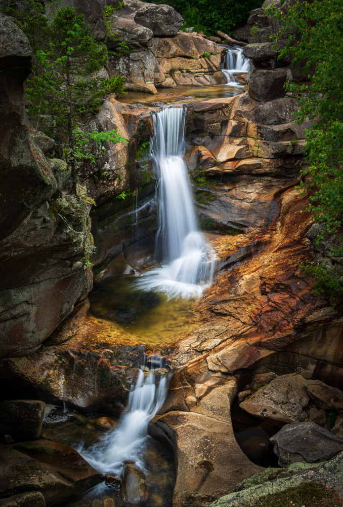 Waterfalls surrounded by trees and big rocks.