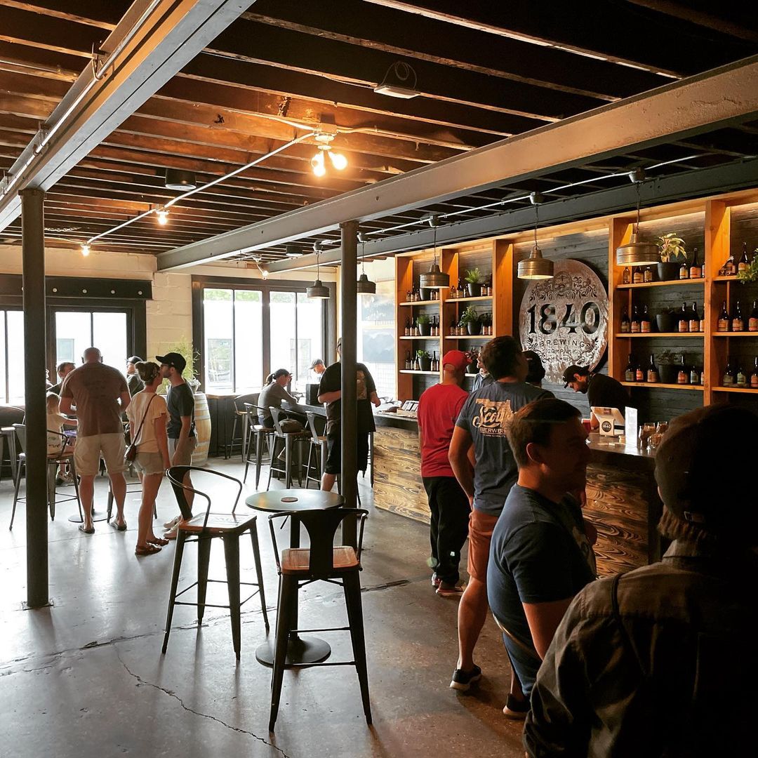 Interior of the brewery with people inside with huge circled board with its logo.