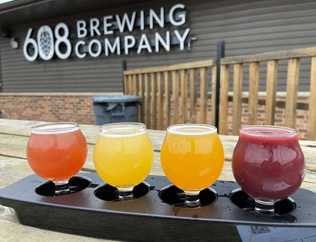 In the main composition there are four glasses full with different flavor beers for tasting and in the background is a huge label on the front of the brewery.