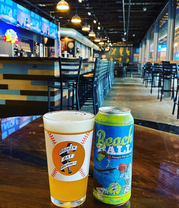 Beer in a glass and colorful can as a main piece in the photo and in the background interior of the brewery.