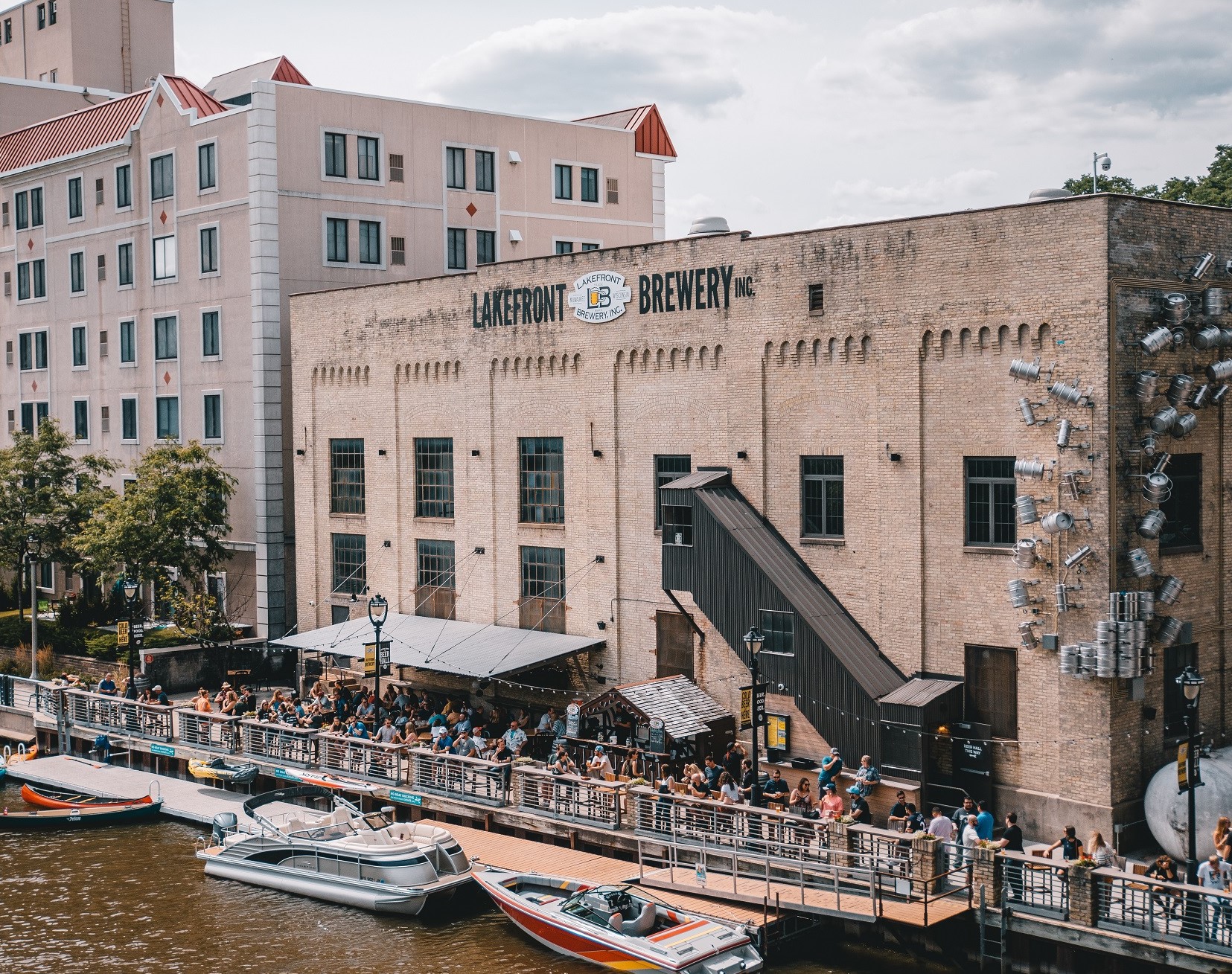 Exterior of the brewery highlighting the front yard next to the boats and water crowded with people.