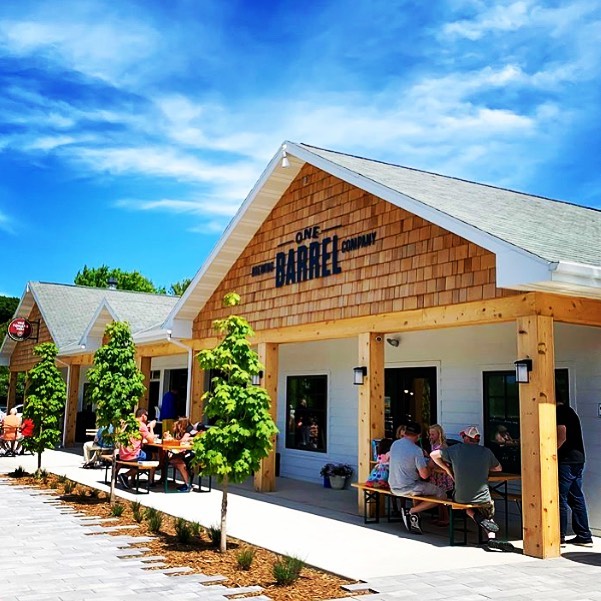 Front of the brewery with lot of wooden details and big written label of the brewery. People sitting and enjoying their beer on the sunny day.