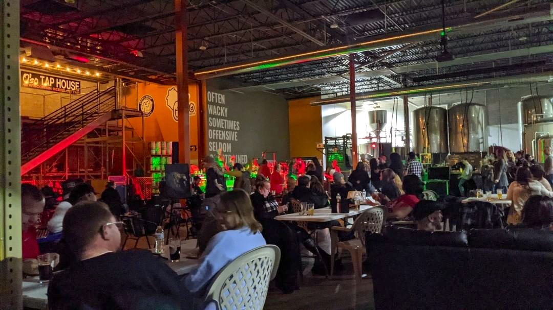 Industrial style interior of the brewery with lost of tables and people enjoying beer and music.
