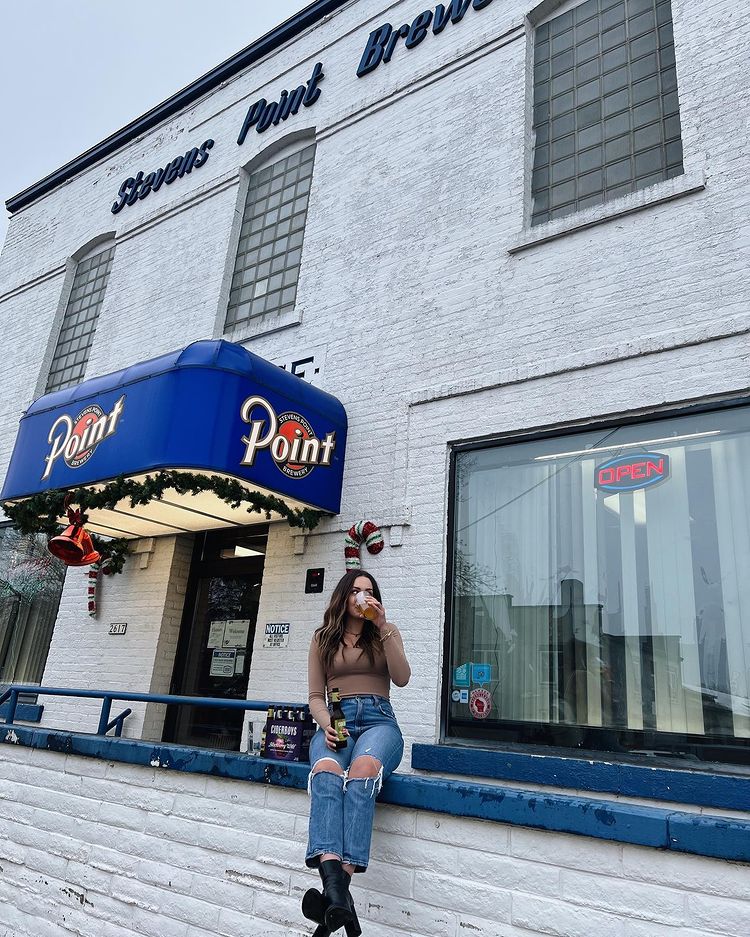 Girl sitting in front of the brewery and drinking a beer while posing.