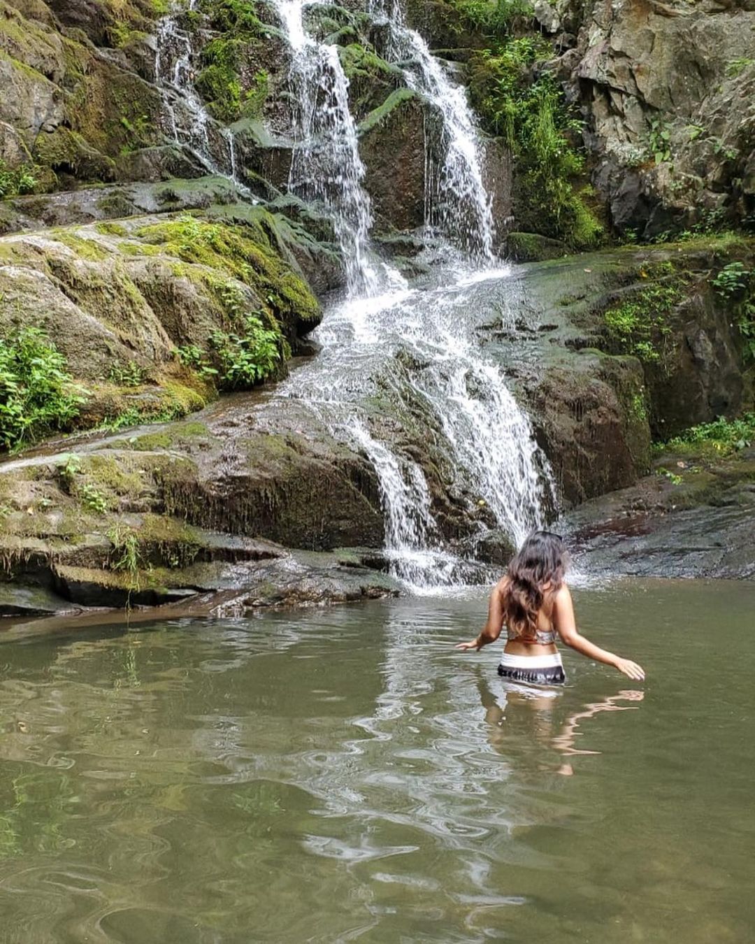 A woman walking in the natural pool of a waterfall.