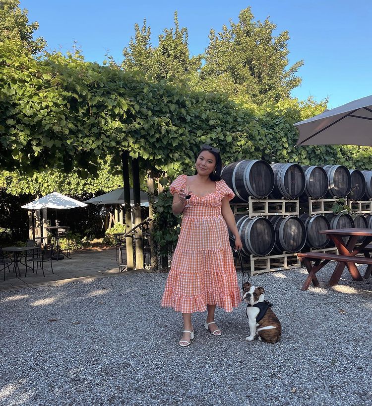 Girl posting with a dog infront of the wooden barrels in front of the beautiful exterior of the vineyard.