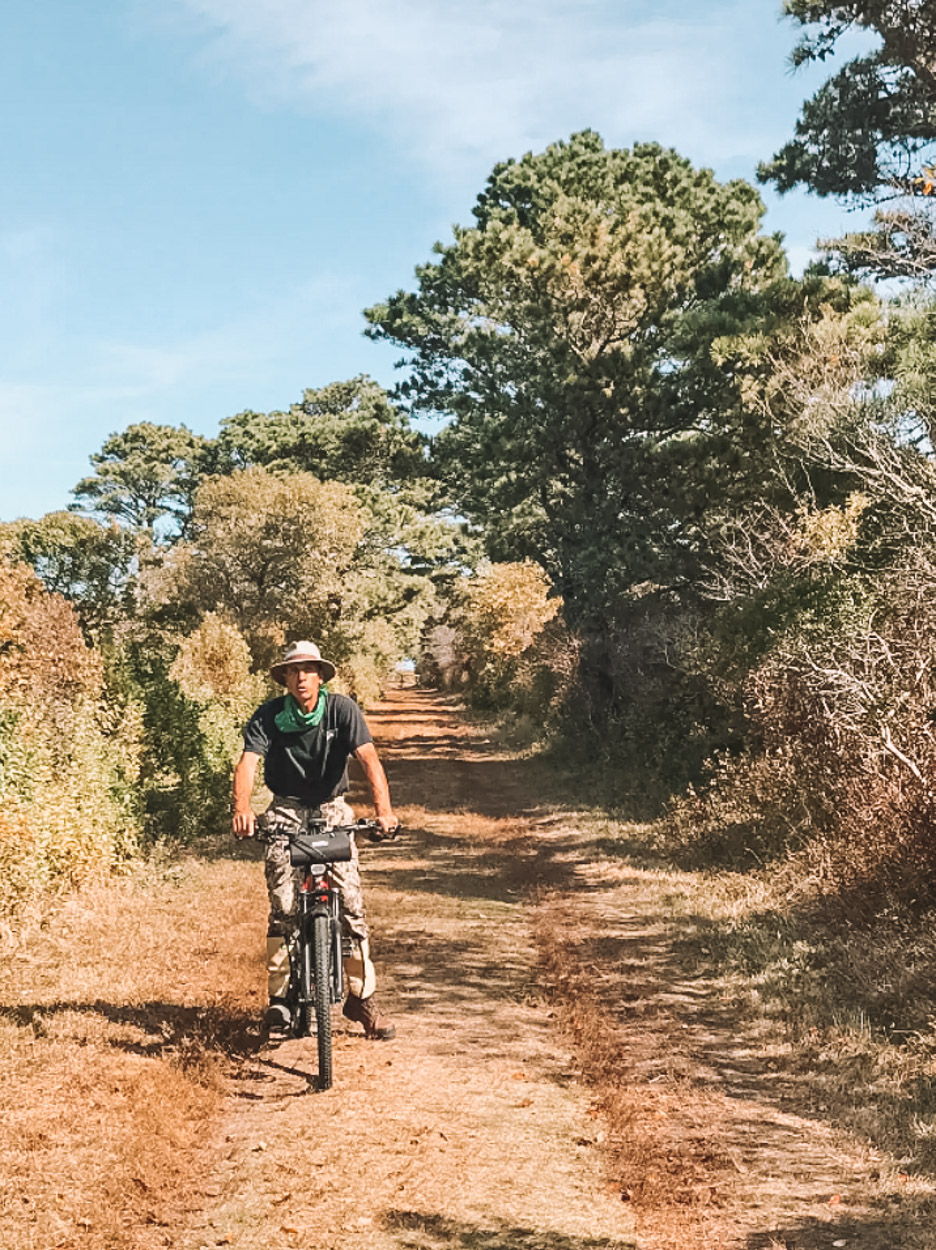 A man riding a bike on a path sandwiched between trees and bushes in Montauk.