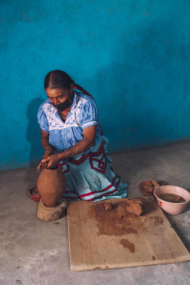 A woman demonstrating a red clay pottery creation.