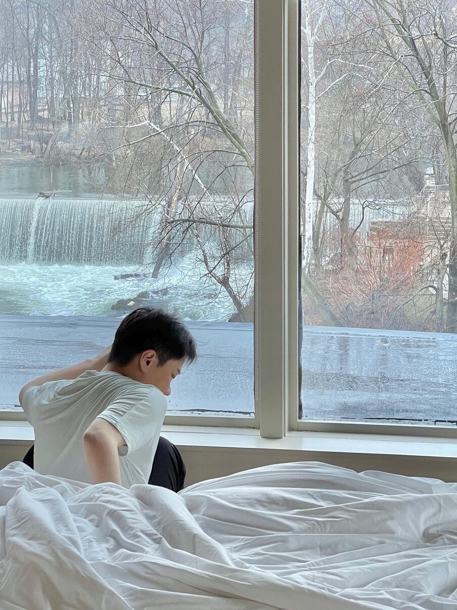 Boy getting out of the red while the beautiful small waterfall is outside de window.