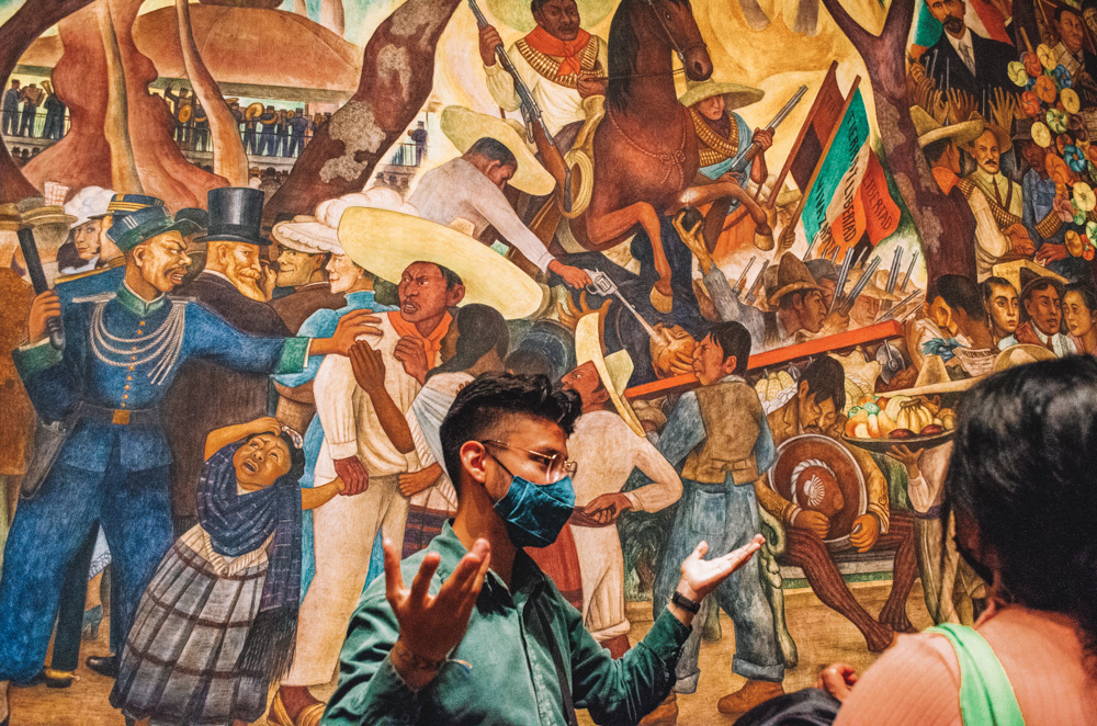 A tour guide discussing an artwork with tourist in Diego Rivera Mural Museum.