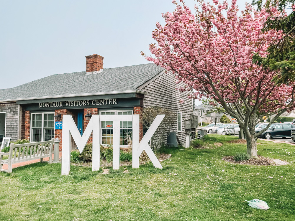 The outside of a visitor center in Montauk with a pink tree and giant white M, T, and K letter signs.