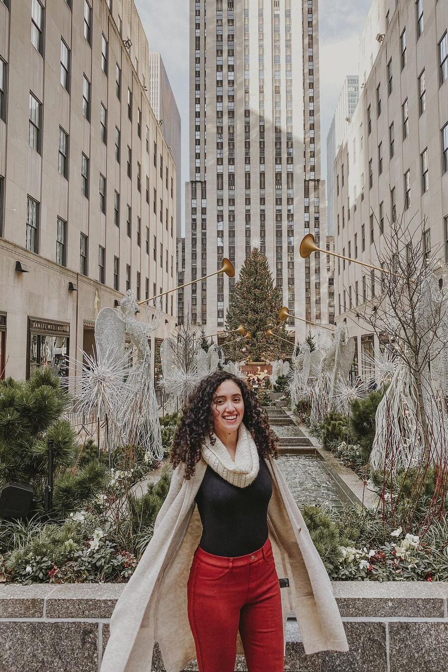 A woman in front of an outdoor area that is surrounded by buildings and decorated with holiday decorations in NYC