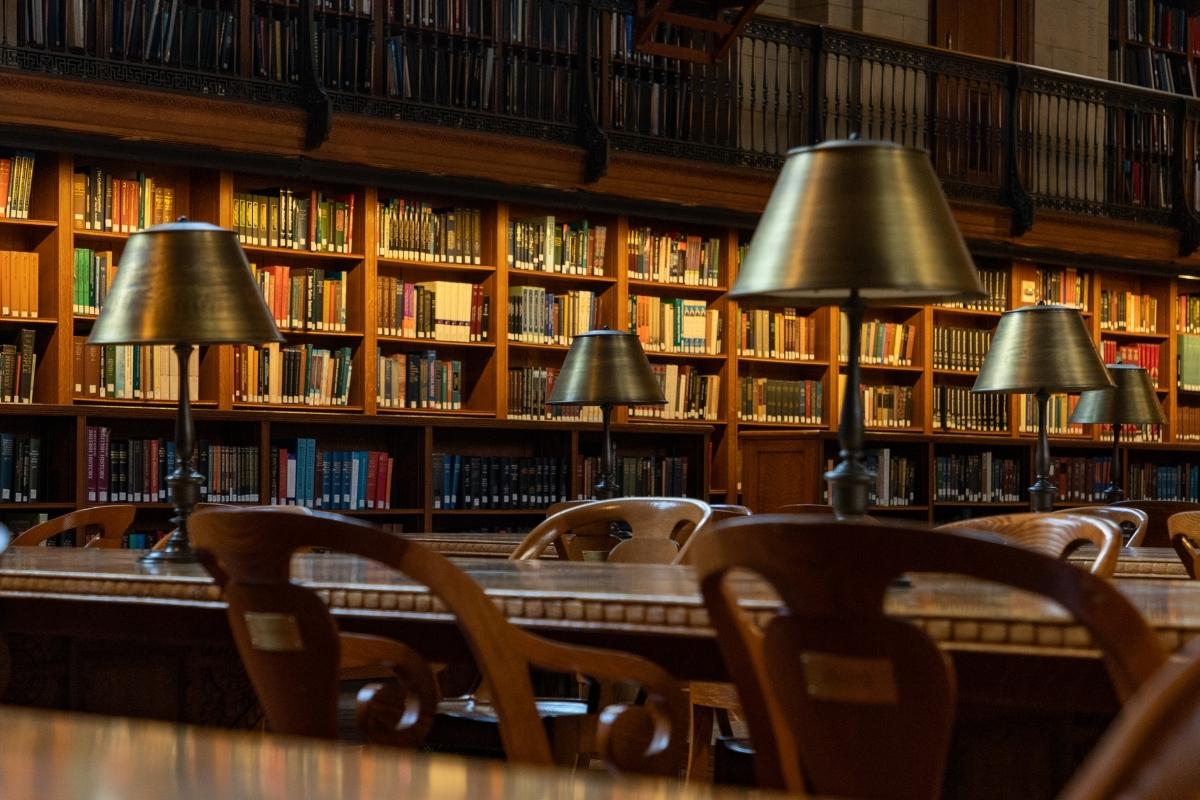The inside of the New York Public Library, featuring bookshelves, lamps, tables, and chairs