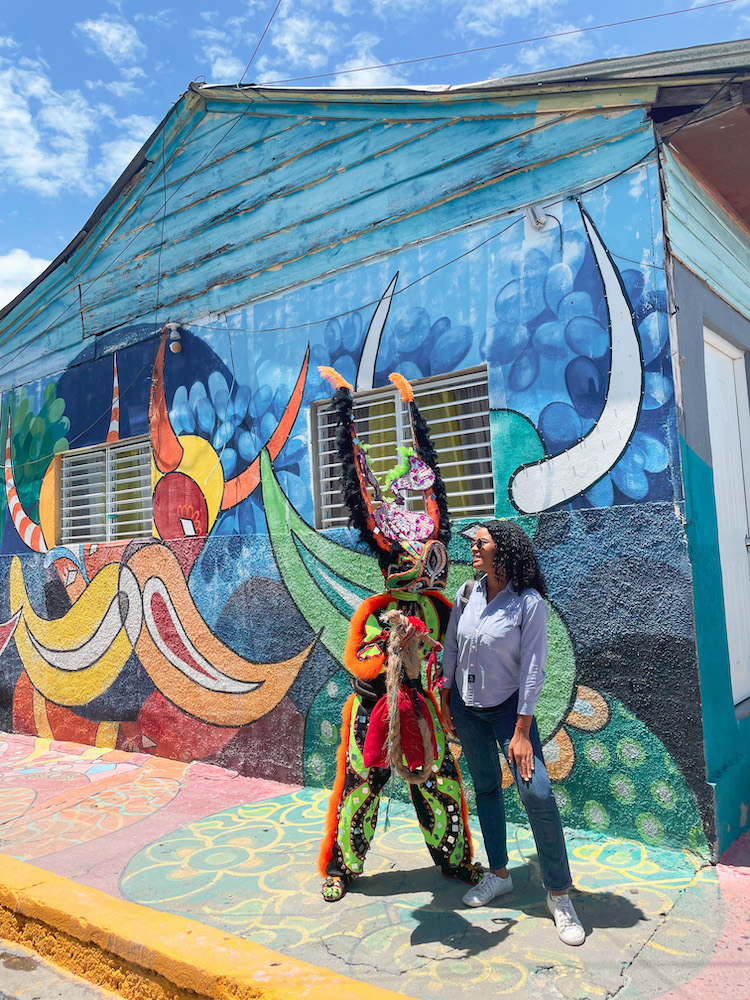 A woman interacting with a person dressed in festival costume in front of a mural in Santiago, Dominican Republic.