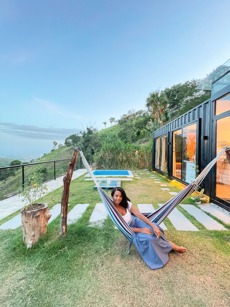 A woman sitting on a hammock outside a shipping container accommodation at the mountains.