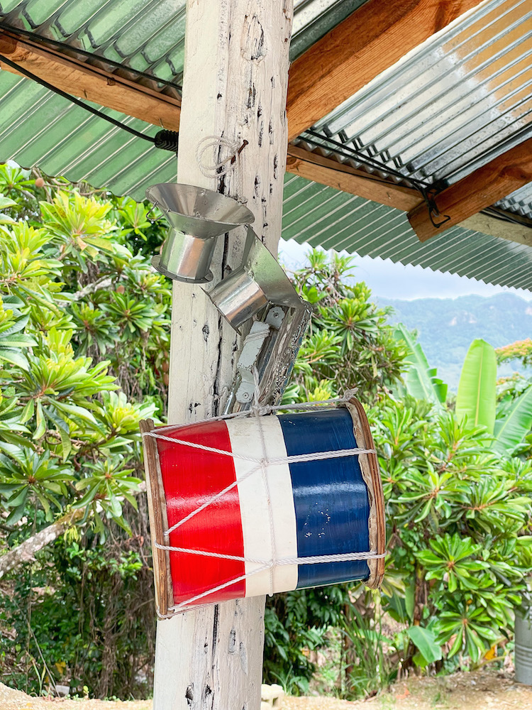 A drum, painted with the colors of the Dominican flag, hanging on a wood.