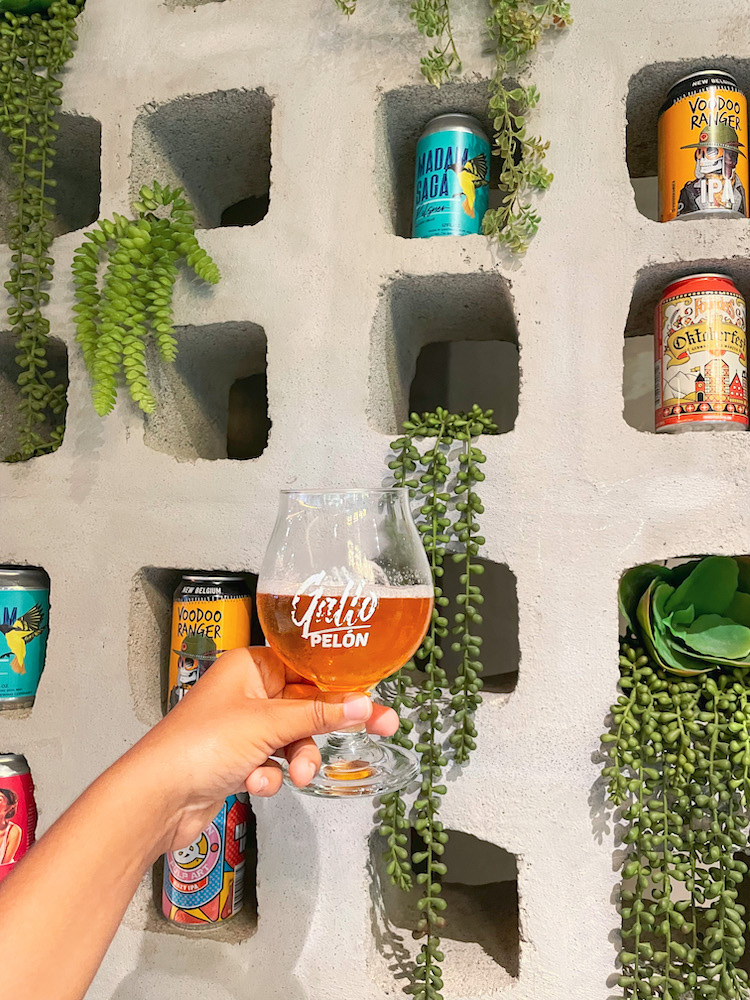 A glass of drink in front of a wall with canned drinks and plants.