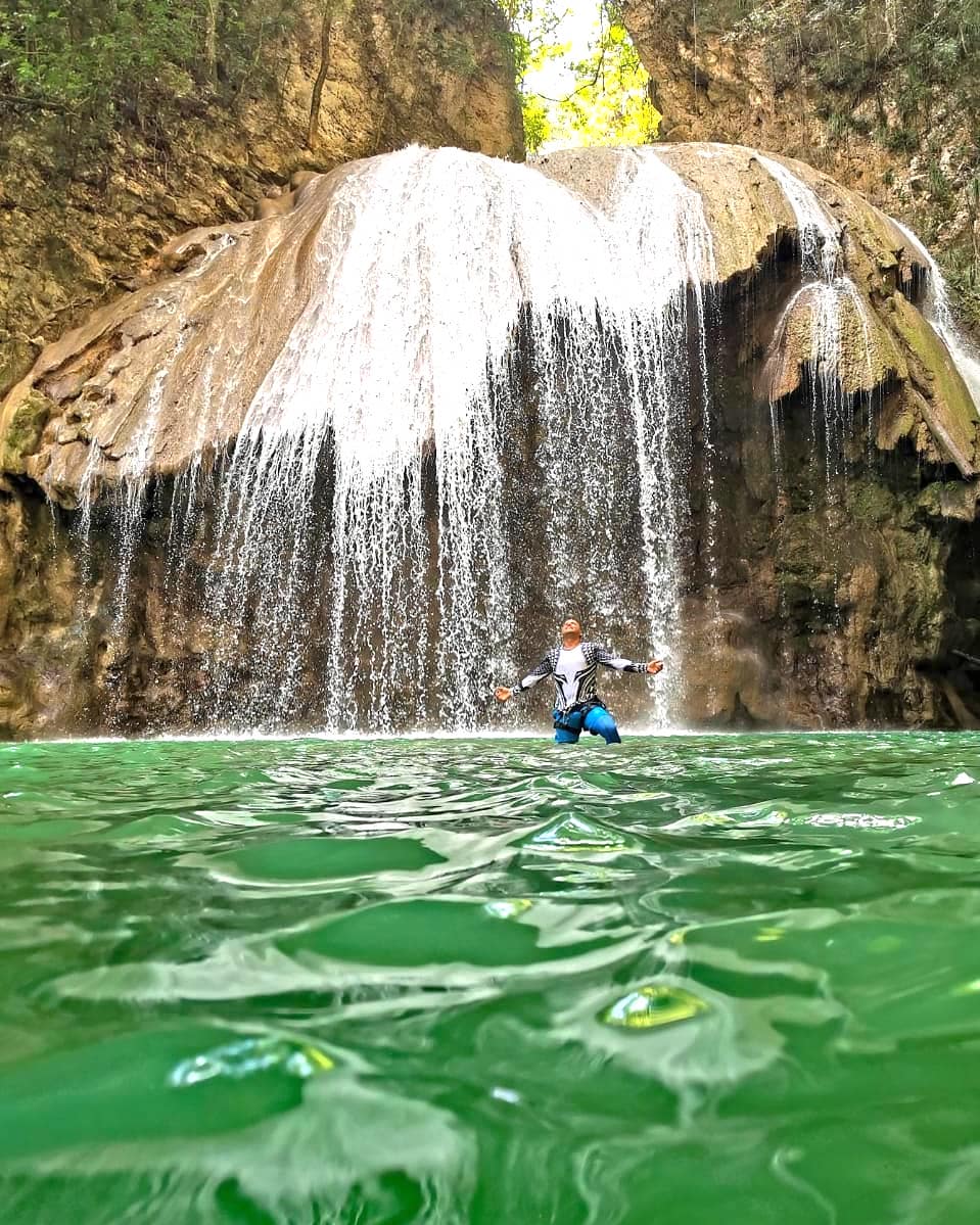 A man at a natural pool under the waterfall.
