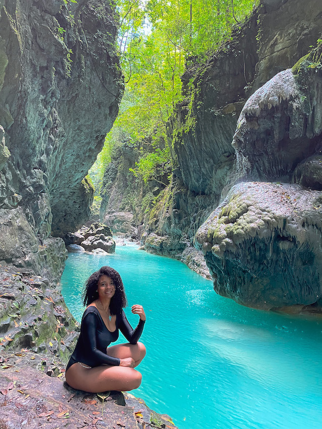 A woman sitting by a natural pool between rock walls at Río Partido.