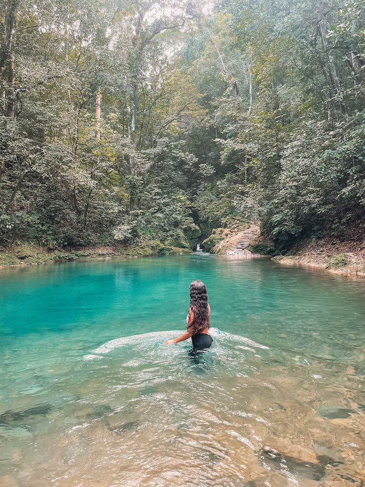 A woman standing at a natural pool surrounded by trees in the Dominican Republic.
